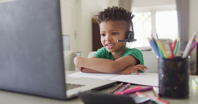 African american boy wearing headphones and having school image call on laptop. Spending quality time at home, childhood, education and learning concept.