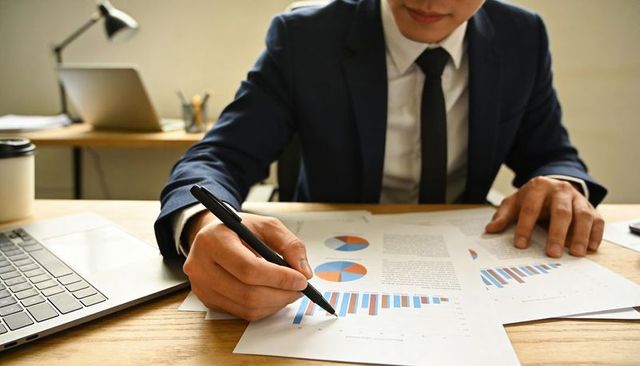 Business Executive Reviewing Sales Reports and Marking Bar Chart with Pen on Office Desk