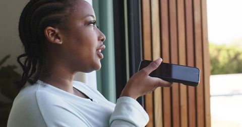 African american woman speaking into smartphone while standing by open door