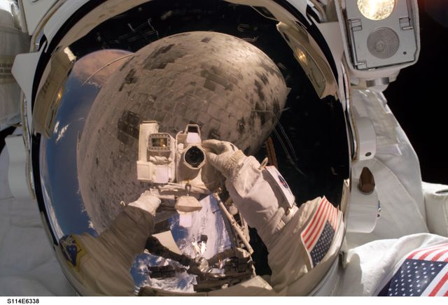 An astronaut is taking a selfie during a spacewalk reflecting the thermal protection tiles on the Space Shuttle Discovery. Perfect for use in publications and content about space exploration, NASA missions, space technology, and human achievements in space. This image captures the juxtaposition of human presence and advanced spacecraft technology.