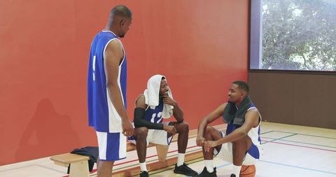Basketball teammates taking break, exchanging fist bumps and bonding on indoor court bench