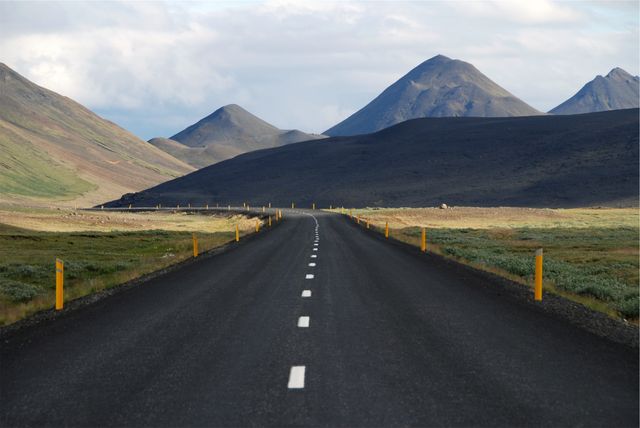 Empty road stretches towards mountains, creating a serene and isolated feel. Ideal for travel blogs, adventure magazines, and promotional materials highlighting road trips, outdoor explorations, or peaceful natural settings.