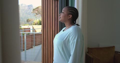 African american woman gazing from sliding door onto hillside balcony, contemplative calm