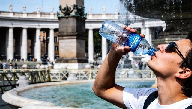 Tourist drinking bottled water by historic fountain in sunlit european plaza