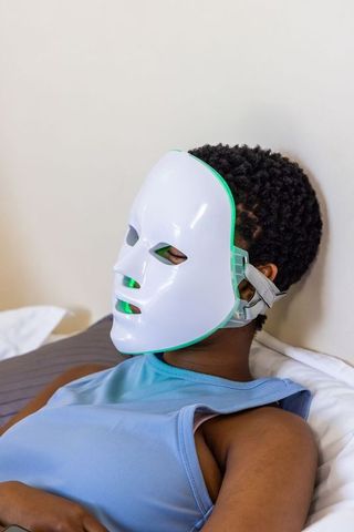 Reclining african woman wearing led facial mask for skincare therapy and relaxation