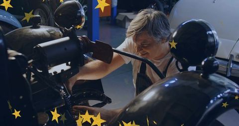Gray-haired mechanic restoring vintage car engine in workshop with gold star accents