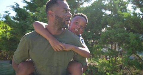African american father giving son piggyback ride in sunlit backyard bonding moment