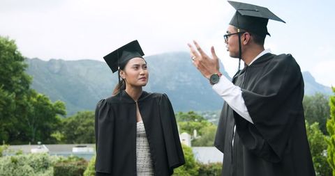 Graduating couple celebrating milestone in cap and gowns outdoors
