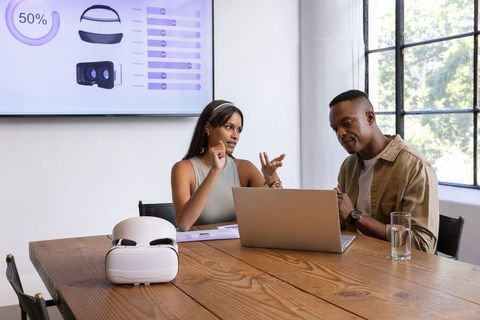 Diverse team discussing vr headset prototype and user data on laptop