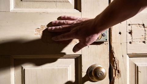 Hand pressing weathered wooden door with chipped paint and brass knob, close-up texture
