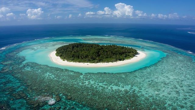 Tropical islet floating inside turquoise lagoon with white sand beach and coral reef