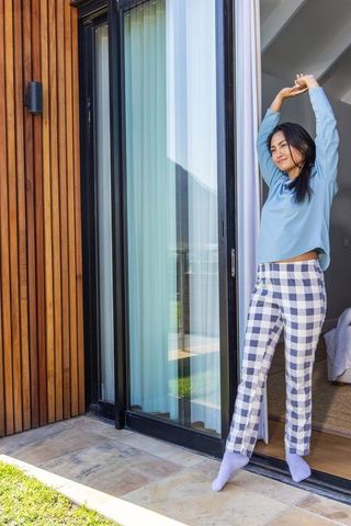 Asian woman stretching in patio doorway wearing gingham pants and cozy socks morning stretch