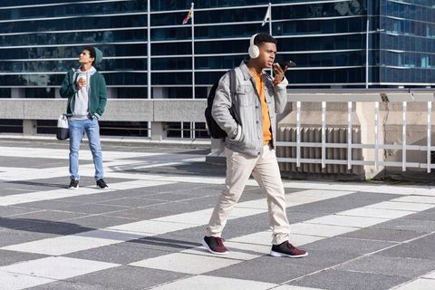 Diverse young man wearing headphones walking on urban rooftop plaza speaking into phone