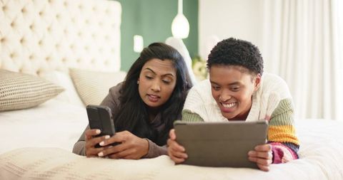 Diverse Friends Relax Using Smartphone and Tablet on Spacious Bed