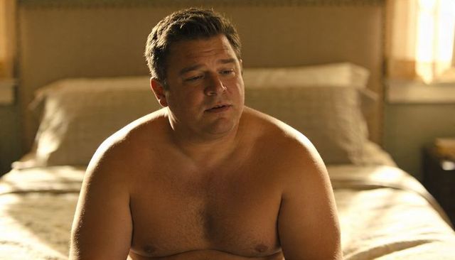 Midlife man waking and reflecting in sunlit bedroom, barechested morning introspection