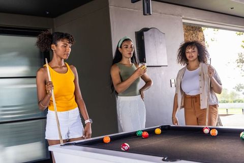 Diverse women playing pool in modern covered game room, social leisure and camaraderie