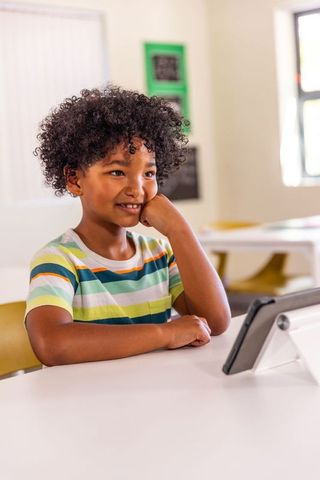 Curly-haired african american boy watching tablet and learning in bright classroom
