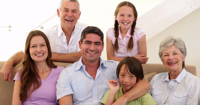 Multi-generational family smiling on a couch at home, comprising grandparents, parents, and children. Suitable for themes related to family bonding, home life, generational connection, happiness, and love within families. Ideal for advertisements, brochures, websites, and publications focusing on family values, home living, and family-related products or services.