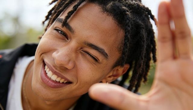 Young man smiling and winking reaching hand to camera close-up outdoor portrait with gold chain