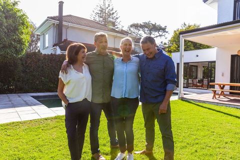 Middle-aged Friends Joyfully Bonding on Lawn Near Modern Home