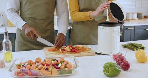 Diverse Couple Prepping Vegetables in Modern Kitchen with Compost Bin