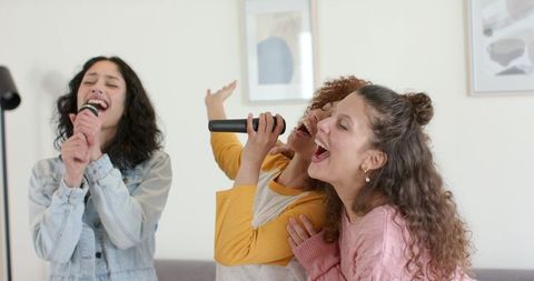 Diverse friends singing karaoke at home, cozy living room trio enjoying music