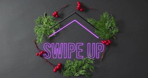 Neon swipe up arrow with holiday pine sprigs and red berries on dark tabletop
