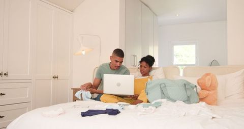 Diverse couple planning vacation while packing on bed