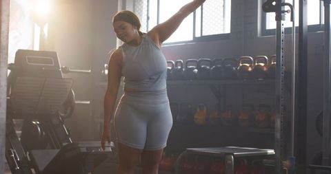 African American Woman Stretching Sideways in Sunlit Gym During Kettlebell Workout