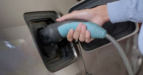 Person Charging Electric Vehicle with Turquoise Connector
