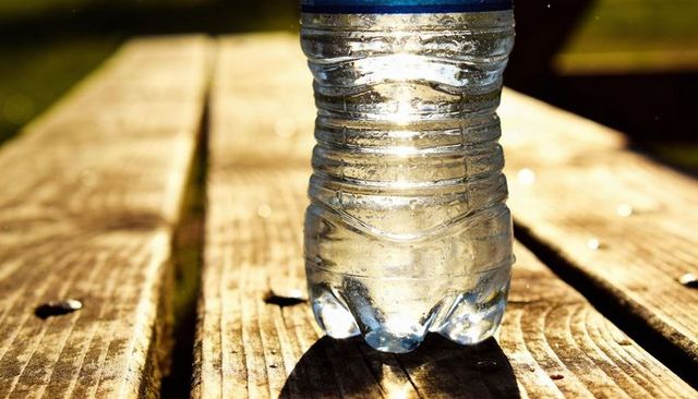 Sunlit water bottle standing on wooden table showing condensation and golden bokeh