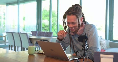 African american podcaster smiling while recording live from bright home studio with mic