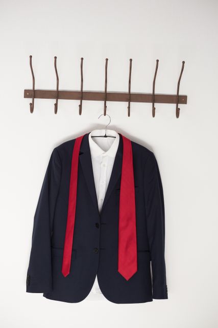 Blazer with red tie hanging on wall hook against white wall. Ideal for illustrating concepts of business attire, professional wardrobe, and office fashion. Suitable for use in fashion blogs, business articles, and organizational tips.
