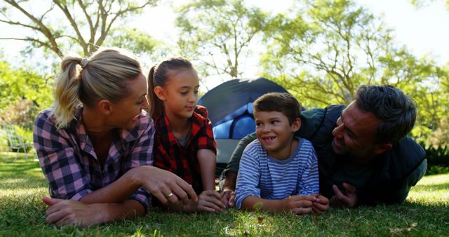 Happy family enjoying time outside on a camping trip lying on grass near a tent. Perfect for advertisements promoting outdoor activities, family travel experiences, nature excursions, summer vacations, or content about family bonding and healthy lifestyles.