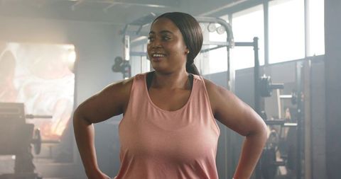 Smiling african american woman standing hands on hips after strength workout in gym