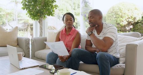 Couple reviewing documents in home setting with laptop