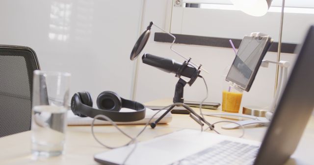 Podcast setup on office desk, featuring microphone on stand, laptop, and headphones, conveys modern remote work environment. Useful for articles on podcasting, remote work tools, and home office productivity.