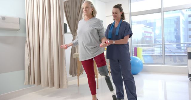 Physical therapist helping senior woman with prosthetic leg during rehabilitation exercise in hospital setting. Ideal for articles on healthcare, recovery, prosthetics, physical therapy, and senior health.