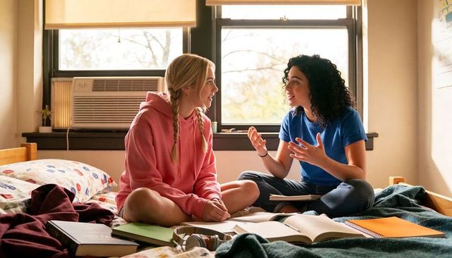 College roommates studying together on dorm bed sharing notes and friendly conversation
