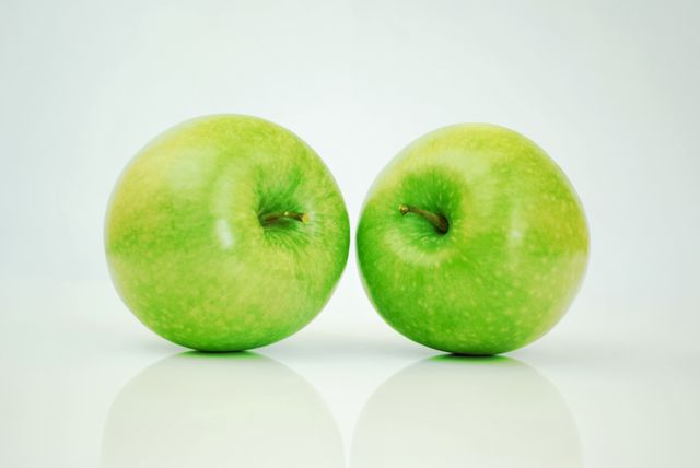 Pair of vibrant green apples with smooth skin on clean white surface, soft gradient background making them stand out. Ideal for health and wellness themes, food blogging, promotional material for organic produce, dieting and nutrition campaigns, and minimalist design projects.
