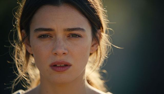 Young woman gazing forward backlit by golden hour, closeup freckled face with rimlight