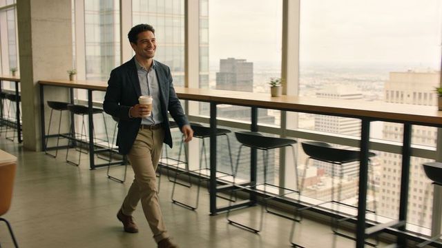 Corporate professional walking with coffee in modern high-rise coworking lounge skyline view