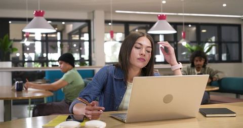 African American woman working on laptop in modern coworking cafe with pendant lights