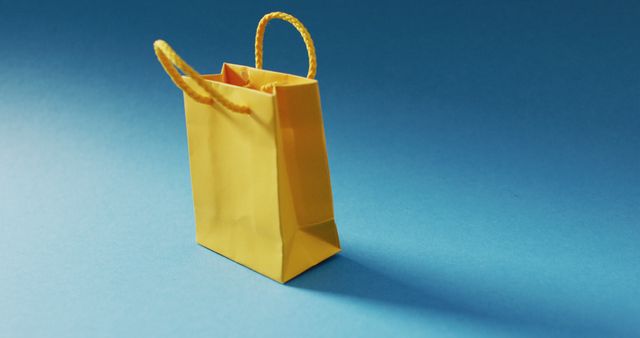 Yellow gift bag with string handles string on blue background. Shopping, sale and retail concept digitally generated image.