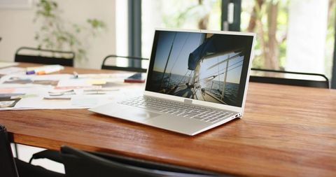 Minimal home office workspace with laptop showing sailboat, wooden table and sticky notes
