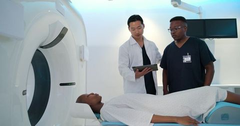 Medical team reviewing ct scan on tablet while patient lying on scanning table in clinic