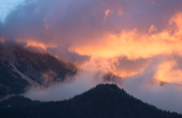 Dramatic shot of a mountain range at sunset with glowing clouds. Ideal for use in travel brochures, nature websites, and posters emphasizing the beauty and grandeur of natural landscapes.