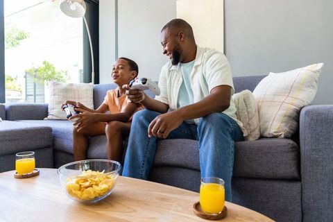 African father and teen son playing video games on sofa, family gaming in living room