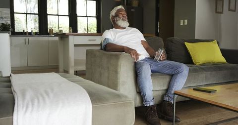 Senior man using blood pressure monitor at home seated on sofa