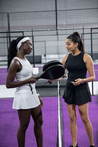Indian and african american women practicing padel on purple court coaching and rivalry